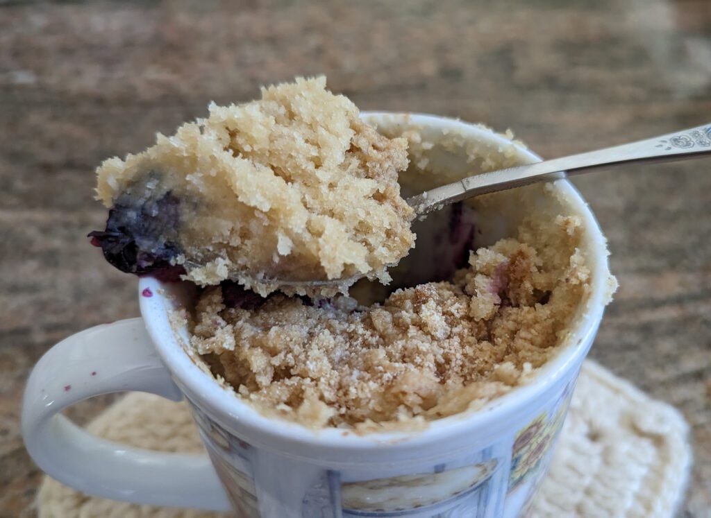 Photo of a blueberrry crumb mug cake with a spoon of cake sitting on top.